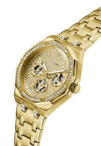 Montre-bracelet en métal doré avec un boîtier octogonal, des accents en strass, un cadran texturé et plusieurs sous-cadrans pour les fonctionnalités de chronométrage.