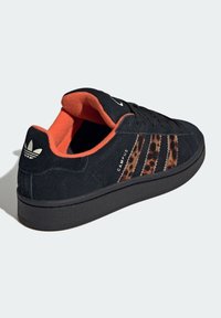 Černé semišové tenisky s oranžovým vnitřkem, s leopardím potiskem na třech pruzích. Černá gumová podrážka a logo Adidas na patě.