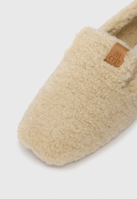 Crijevo boje kreme, plišani papučasti lofer sa kožnom etiketom s utisnutim slovima "M O P" blizu gornjeg otvora.