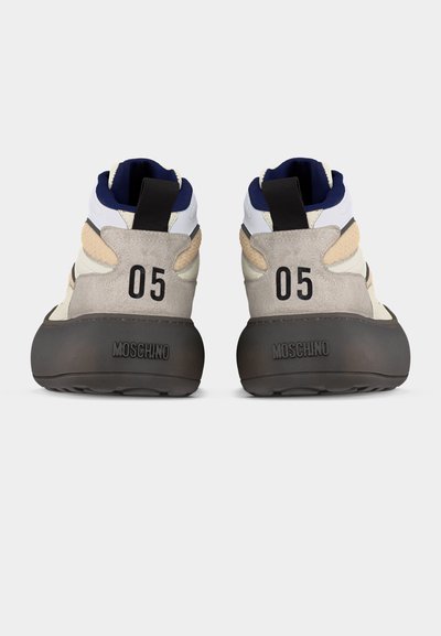 Pár béžovo-bielych tenisiek Moschino s čiernymi podrážkami, tmavomodrým vnútrom, pútkami na ťahanie a číslom "05" potlačeným na päte oboch topánok.