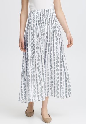 Kvinde iført ankel-lang hvid nederdel med lodrette grå mønstrede striber, kombineret med beige spidse ballerinaer og hvid ærmeløs top.