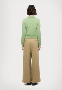 Grøn strikket sweater med krave, tætsiddende ved taljen. Parret med brede beige bukser. Sorte sko med en kraftig sål.