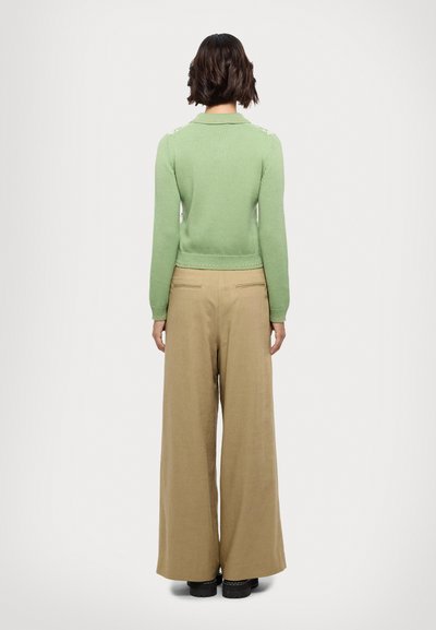Maglione verde a maglia con colletto, aderente in vita. Abbinato a pantaloni beige larghi. Scarpe nere con suola spessa.