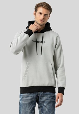 Hoodie gris clair avec accents noirs, cordons de serrage et poche avant. Présente un logo imprimé sur la poitrine. Tissu doux avec des poignets côtelés.