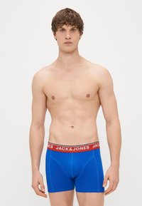 Blue boxer briefs with red elastic waistband featuring "JACK & JONES" logo. Smooth cotton material, fitted design, and short leg length.