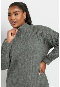 Maglione grigio a coste con zip, colletto alto, maniche lunghe e vestibilità rilassata. Presenta una trama sottile e dettagli della zip in evidenza.