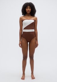 Pántnélküli egyrészes fürdőruha geometrikus színblokkoló mintával, barna és fehér színekben, sima textúrával és minimalistán formával.