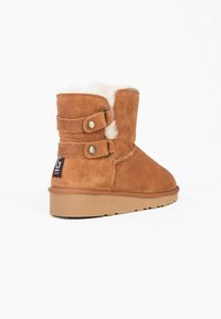 Stivali alla caviglia in suede beige con due cinturini decorativi e bottoni dorati, dotati di una morbida fodera interna e suola in gomma.