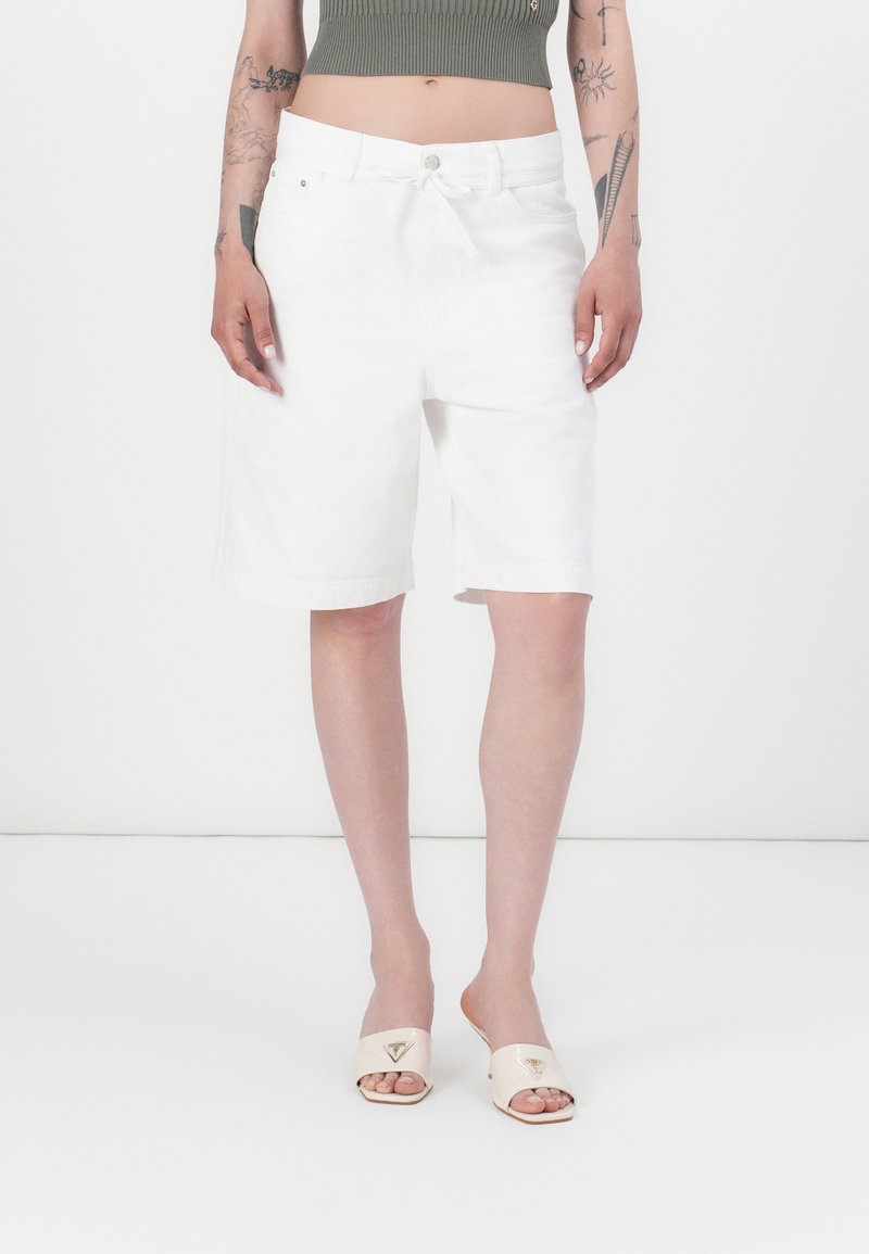 Hvite denimshorts med avslappet passform, med knapp- og snoråpning og oppbrettede kanter. Brukt med kremfargede sandaler.
