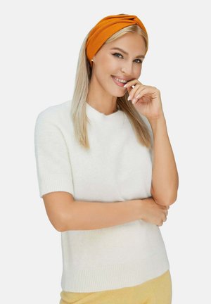 Maglione corto a maniche corte di colore bianco con una texture morbida. Il modello indossa una fascia per capelli arancione annodata. Lo sfondo è bianco uniforme.