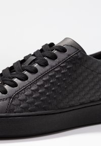 Sneaker in pelle nera con superficie texture e un motivo a logo ripetitivo, lacci tondi e suola in gomma nera solida.