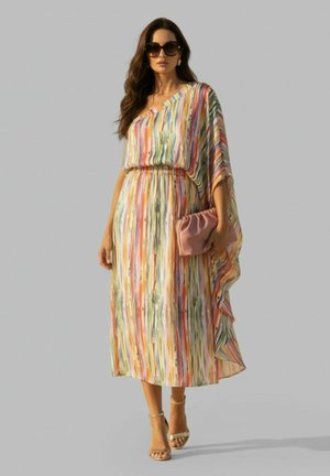 Vrouw draagt een kleurrijke gestreepte midi-jurk met één schouder, beige enkellaarsjes met riempje, oversized zonnebril en houdt een roze clutch vast.