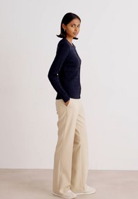 Navy cable-knit long sleeve top paired with light beige wide-leg trousers; features a fitted silhouette and casual sneakers.