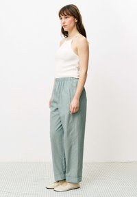 Hellgraue, strukturierte weite Hosen mit einem elastischen Bund, kombiniert mit einem figurbetonten weißen Tanktop; schlichte, neutrale Schuhe runden den Look ab.