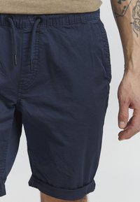 Shorts bleu marine en tissu léger, dotés d'une taille élastique avec cordon de serrage, de poches latérales et de ourlets repliés.