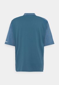 Polo à manches courtes avec un dos teal uni et des manches et col en chambray bleu, présenté de dos.