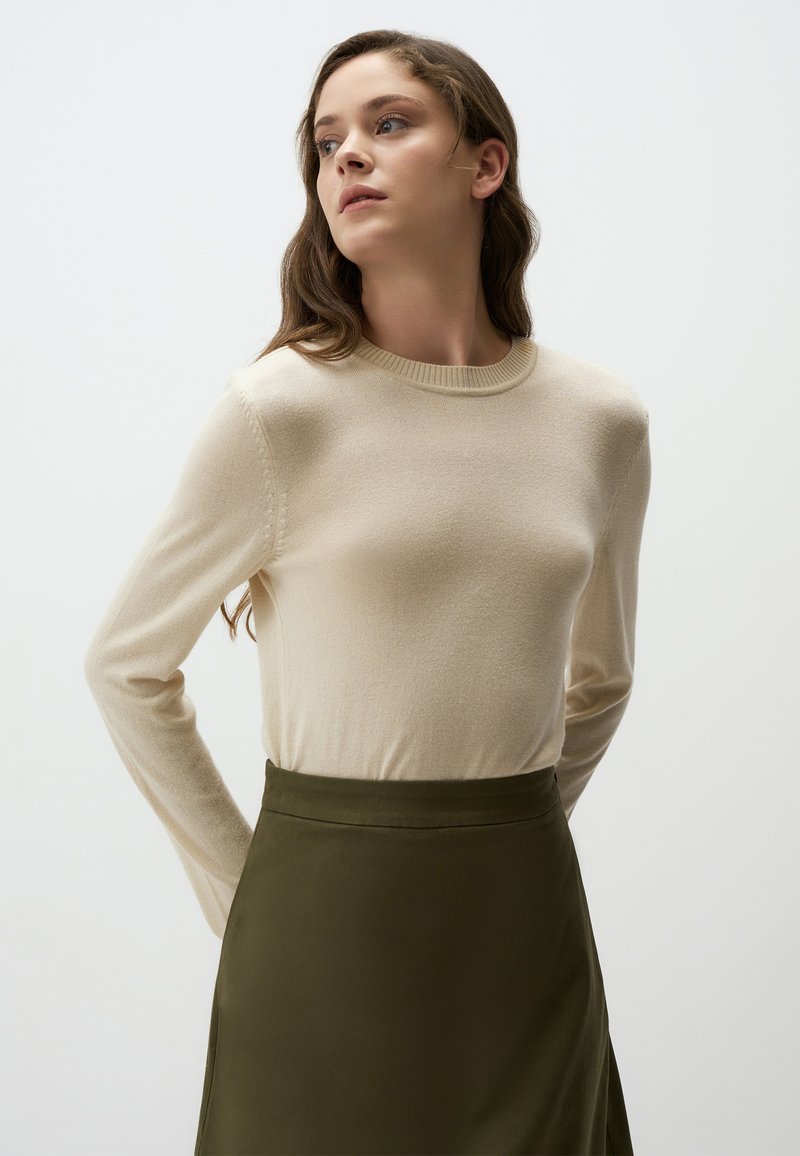 Maglione beige a maniche lunghe con collo rotondo e texture a maglia, abbinato a una gonna verde oliva, caratterizzato da una finitura liscia e un fit sartoriale.