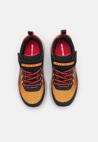 Une paire de baskets Skechers noires et orange avec des accents rouges, des lacets rouges et une sangle de logo, vue de dessus sur un fond blanc.