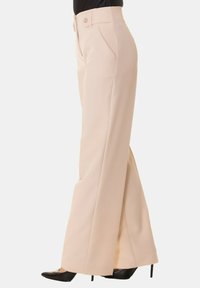 Pantaloni beige a gamba larga realizzati in tessuto liscio, con vita alta, tasche frontali e una piega netta lungo le gambe.