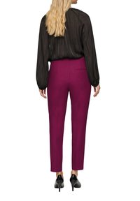 Blouse noire transparente à manches longues avec des rayures verticales, associée à un pantalon ajusté rose foncé. Le pantalon possède une poche arrière et un design fuselé.
