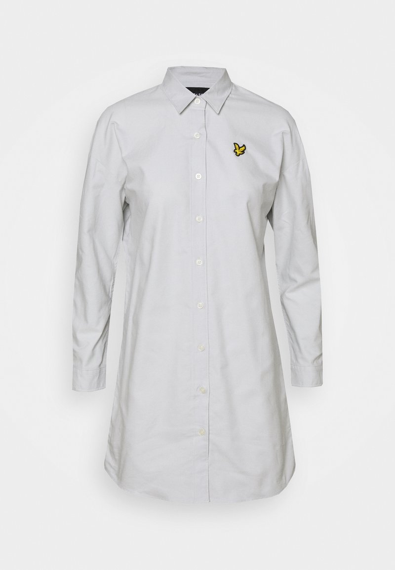 Robe-chemise blanche à manches longues avec col pointu et petit logo d'oiseau jaune sur le côté gauche de la poitrine.