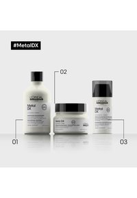 Tre hårpleieprodukter: en høy hvit sjampo-flaske, et rundt hvitt maske-krukke, og en slank svart og hvit spray, alle merket "Metal DX."