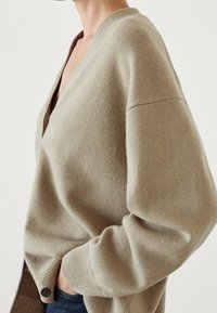 Beige cardigan featuring a V-neck, dropped shoulders, ribbed cuffs, and a button closure, made from soft, textured knit fabric.