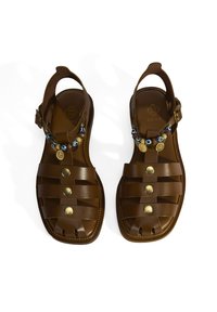 Braune Leder-Sandalen mit einem Riemendesign, metallischen Akzenten und dekorativen Perlen auf der Vorderseite. Glatte Textur und offene Zehen.