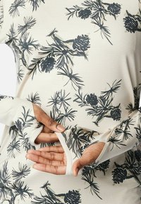 Hände, die die Daumenloch-Ärmel eines beigen Langarmshirts mit schwarzem und grauem Blumenmuster zeigen.