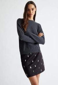 Maglione grigio a maglia con maniche lunghe, abbinato a una gonna nera aderente decorata con abbellimenti argentati sparsi.