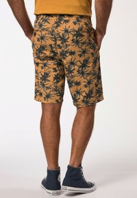 Beige korte broek met zwarte bladerenpatronen, met een casual snit en zakken, gedragen met marineblauwe hoge sneakers.