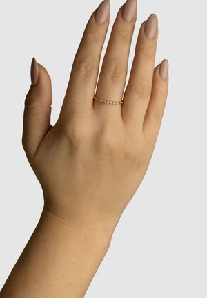 Gold ring featuring a delicate band set with small, clear stones. Shiny surface with a smooth finish, worn on a hand with neutral nail color.