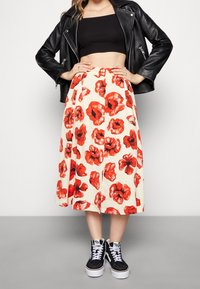 Kukkakuvioinen midihelmainen hame, jossa on kermaan vivahtava pohjaväri ja punaisen unikon kuviot, yhdistetty mustaan lyhytmalliseen toppiin ja mustiin korkeavartisiin tennareihin. Nahkatakki pidetty auki.