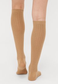 Knee-high sokid heledas tanis, ribiga tekstuuri ja elastse paelaga ülevalt. Pehme materjal ja õmblusteta varvaste disain.