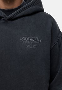 Felpa con cappuccio grigia scura, caratterizzata da una texture morbida, tasca a marsupio e dettagli del logo ricamati in un colore contrastante sul petto.