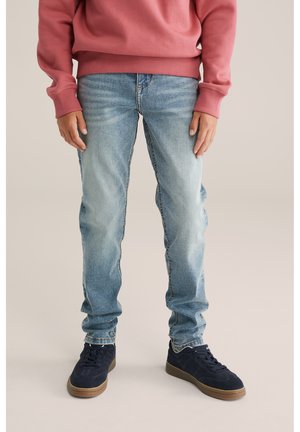 Lichtblauwe denim jeans met een rechte pasvorm, vervaagd in het bovenbeen, gecombineerd met marineblauwe sneakers en een roze sweatshirt.