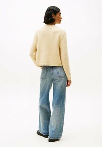 Beige cropped sweater met een gestructureerde brei, gecombineerd met hooggetailleerde lichtblauwe wijde jeans, gezien vanuit de achterkant.