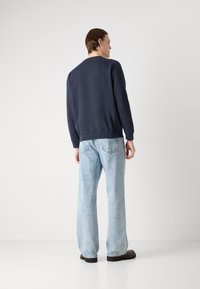 Sweatshirt azul-marinho com mangas longas, punhos e bainha canelados. Combinado com jeans de corte solto de um azul claro e sapatos pretos robustos. Design simples.