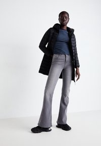 Černá péřová bunda s kapucí, námořnický pruhovaný top a rozšířené šedé džíny. Černé tenisky dokončují outfit. Jednoduchý design, hladká textura.