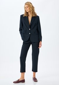 Navyblauw op maat gemaakt blazer met twee grote witte knopen, voorzien van een enkele borstzak en gecombineerd met bijpassende tapered broeken.