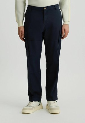 Marineblau cargo-Hosen mit mehreren Taschen, einem Knopf- und Reißverschluss, sowie einem geraden Bein. Kombiniert mit hellen Sneakers.