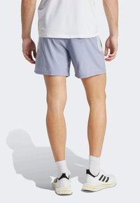 Pantalones cortos deportivos de color gris claro con una cintura elástica, fabricados en un material suave. Combinados con zapatillas blancas que tienen rayas negras y suelas texturizadas.
