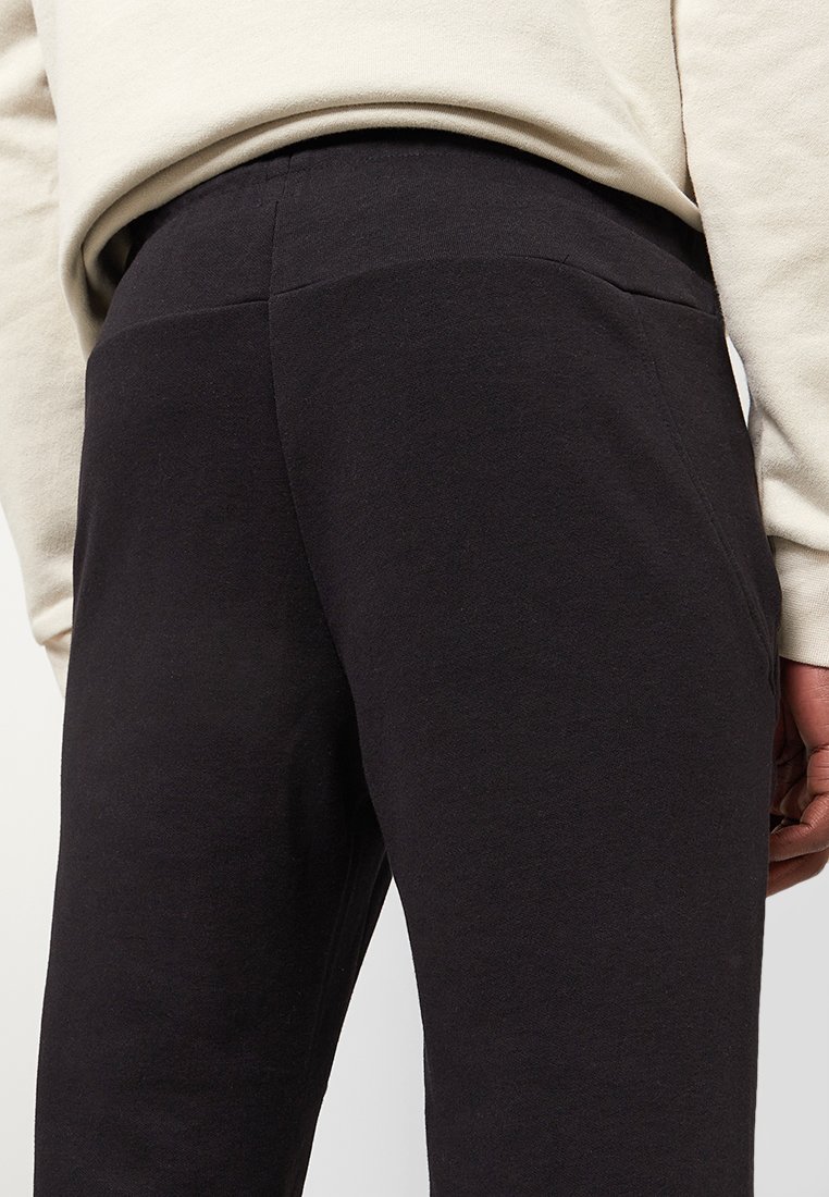 Joggers negros de mezcla de algodón con cintura elástica y bolsillos laterales, que presentan una textura suave y un diseño estilizado.