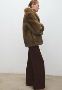 Brown faux fur coat with a wide collar, paired with high-waisted, dark brown corduroy pants. Soft texture and oversized fit.