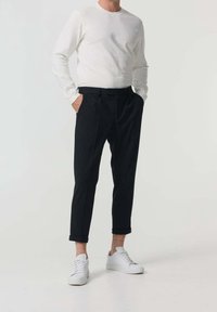 Chemise blanche à manches longues, pantalon plissé noir et baskets blanches. Tenue décontractée avec les revers des pantalons retroussés et des éléments de design simples.