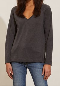 Grå långärmad t-shirt med V-ringning, tillverkad av mjukt jersey-material, med en avslappnad passform och sidoklyftor i fållen.