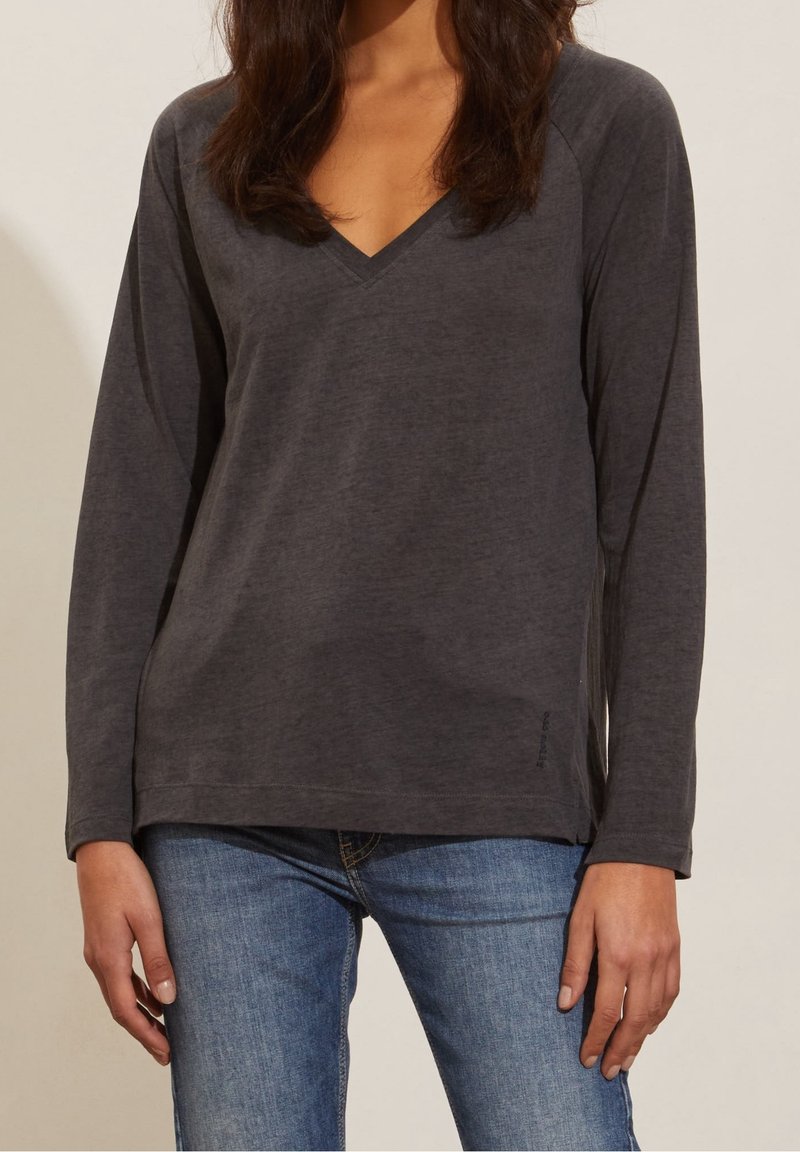 Grå långärmad t-shirt med V-ringning, tillverkad av mjukt jersey-material, med en avslappnad passform och sidoklyftor i fållen.