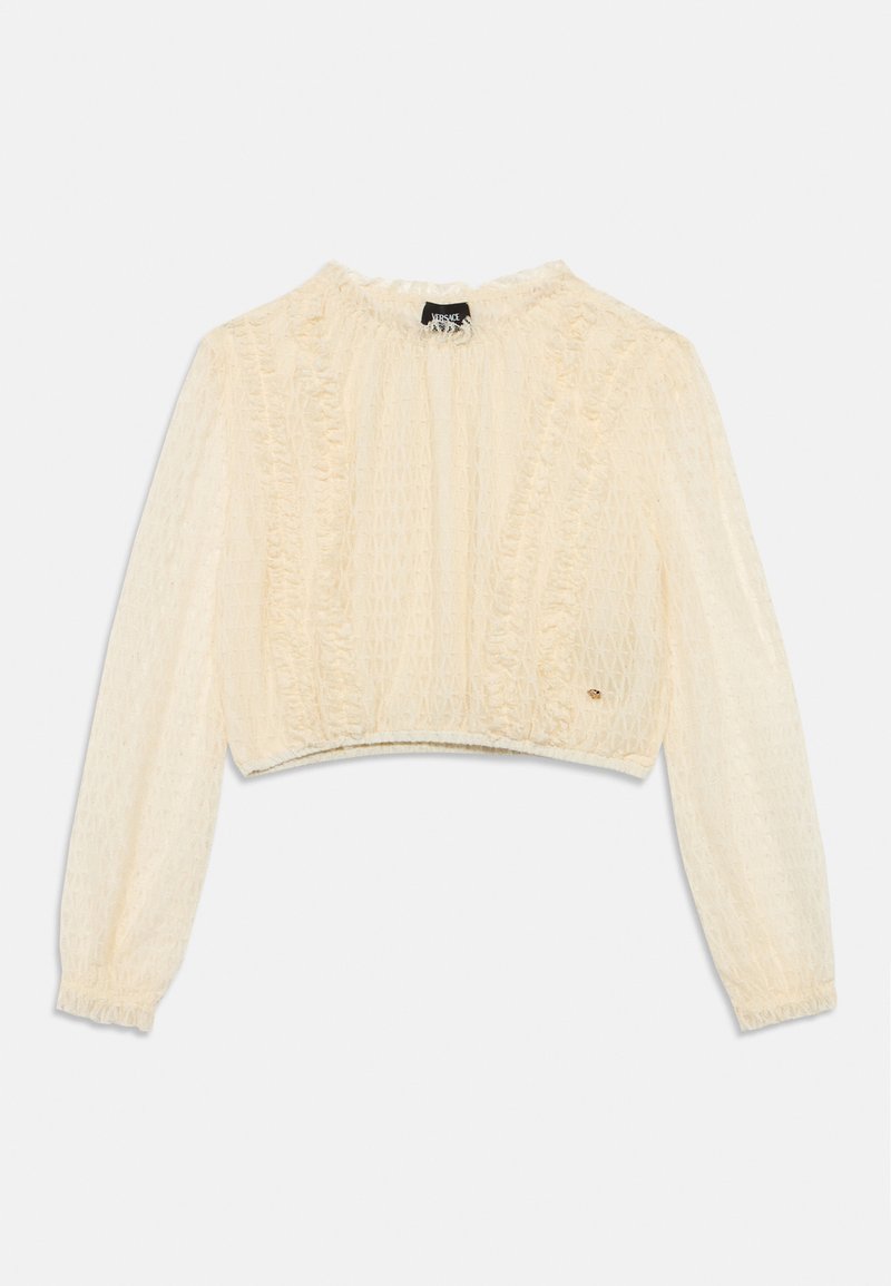 Κοντό μπεζ-κρεμ τοπ μακρυμάνικο με υφή υφάσματος σε σχέδιο ρόμβου και βολάν στα περιγράμματα του λαιμού και στις ραφές.