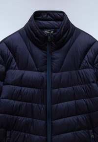 Navy modrá vycpaná bunda s vysokým límcem, která má centrální zip a prošívaný diamantový vzor na látce. Texturovaný nylonový materiál.