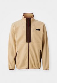 Beige fleece jacket with a high collar, front zip closure, brown accents, two side pockets, and a small logo label on the chest.